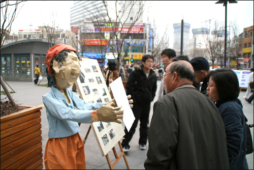 전시물 앞에 모여 내용물을 자세히 읽어 보고 있는 시민들 